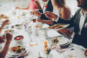 Hochzeitsgäste verteilen das Essen im Familienstil, während sie an einem langen, vollständig gedeckten Tisch sitzen.