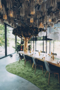 Großer Holztisch mit Mini-Lichtern und Weingläsern dekoriert. Über dem Tisch sind Wolken und am Ende ein Baum voller Lichter.