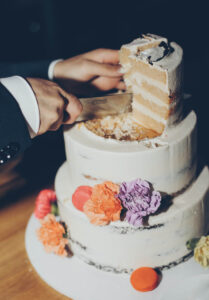 Der Bräutigam schneidet die dreistöckige, mit bunten Blumen bedeckte Hochzeitstorte an.